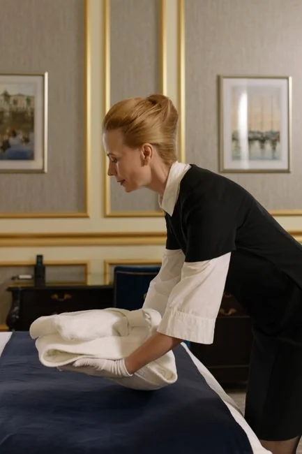 Side view of young male employee holding stack of white towels while standing in bathroom of luxury hotel